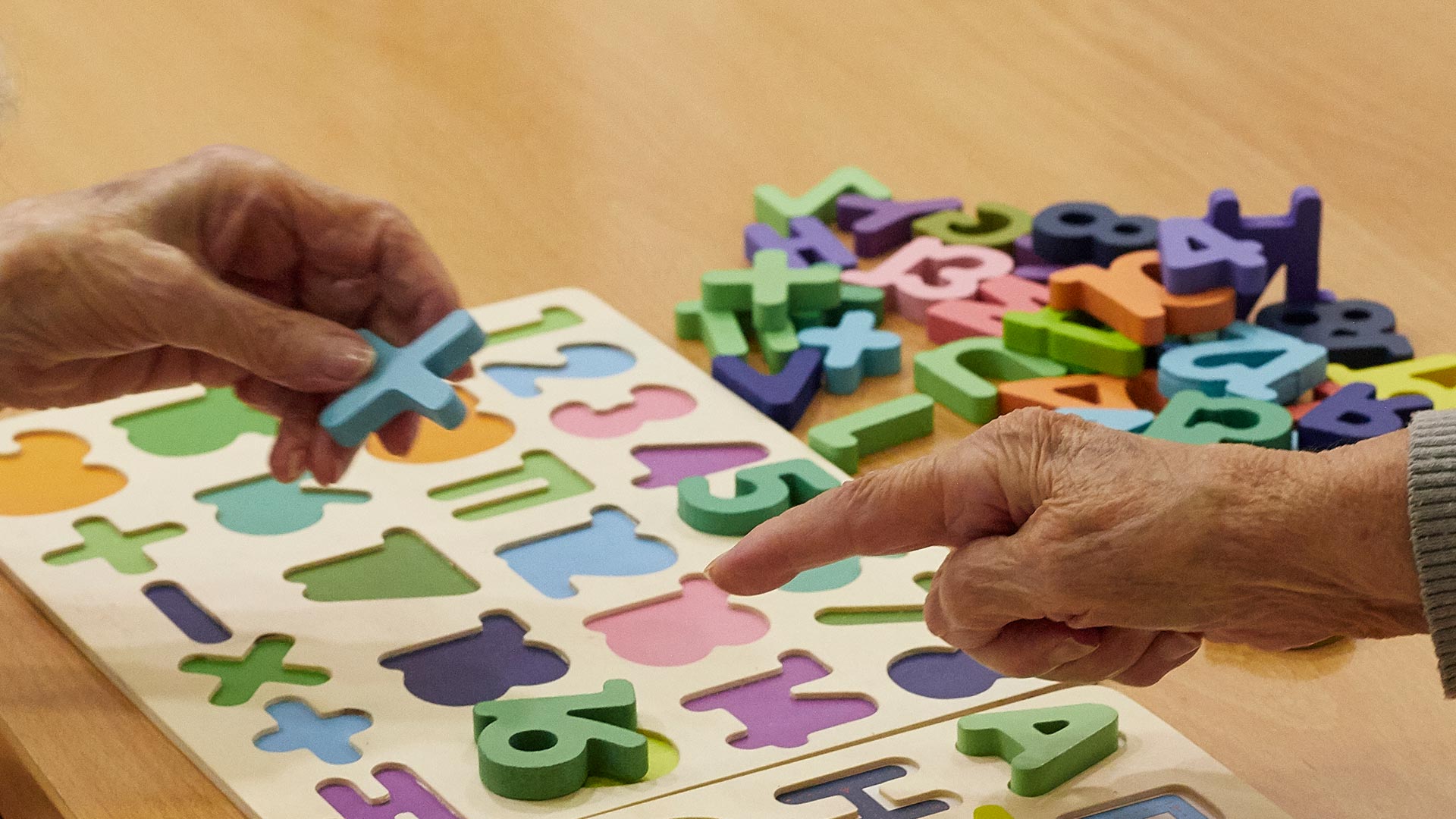 dos manos de personas mayores con un juego en el que colocar números y letras de colores en su respectiva casilla