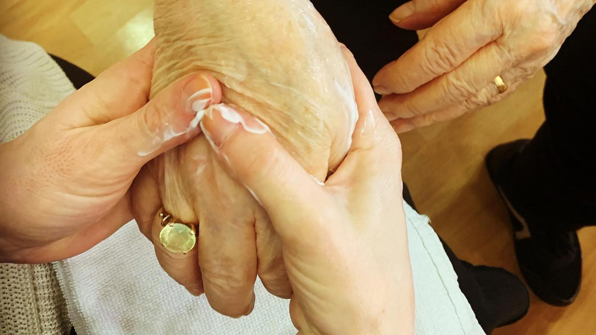 cuidadora aplicando crema hidratante a la mano de una persona mayor